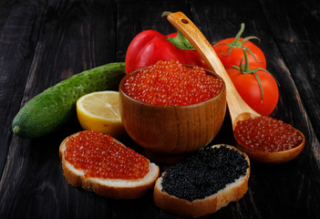 red and black caviar on wooden cup and vegetables on black wooden background