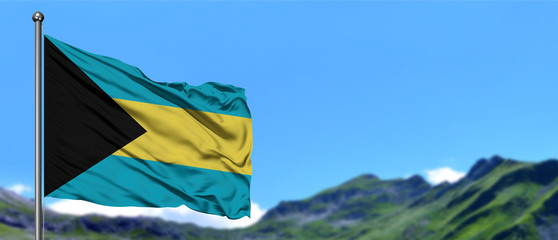 Bahamas flag waving in the blue sky with green fields at mountain peak background. Nature theme.