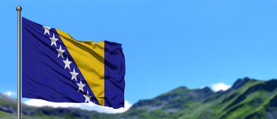 Bosnia Herzegovina flag waving in the blue sky with green fields at mountain peak background....