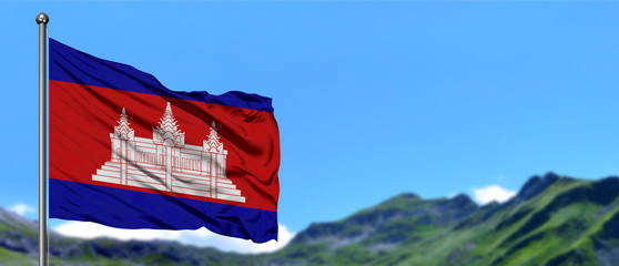 Cambodia flag waving in the blue sky with green fields at mountain peak background. Nature theme.
