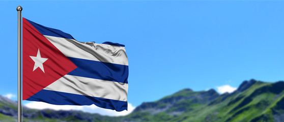 Cuba flag waving in the blue sky with green fields at mountain peak background. Nature theme.