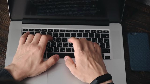 a male programmer in a black shirt is working at a laptop, close-up of the program code and developer's hands on a laptop. modern young programmer sitting at a wooden table at a computer