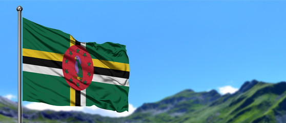 Dominica flag waving in the blue sky with green fields at mountain peak background. Nature theme.