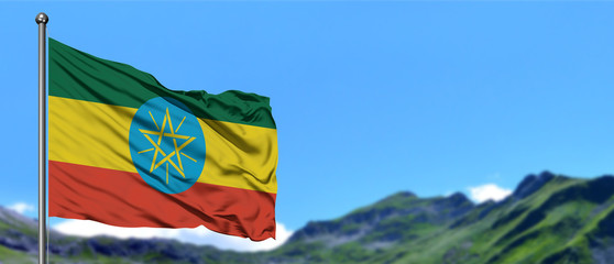 Ethiopia flag waving in the blue sky with green fields at mountain peak background. Nature theme.