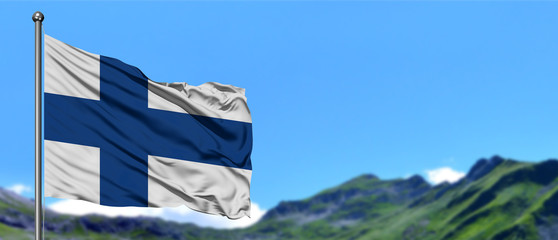 Finland flag waving in the blue sky with green fields at mountain peak background. Nature theme.