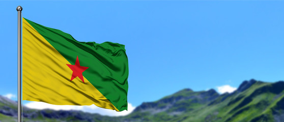 French Guiana flag waving in the blue sky with green fields at mountain peak background. Nature theme.