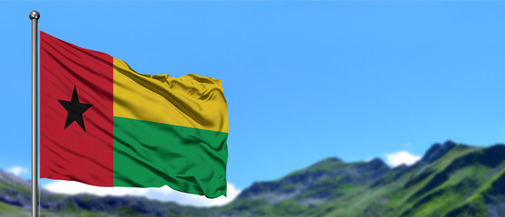 Guinea Bissau flag waving in the blue sky with green fields at mountain peak background. Nature theme.