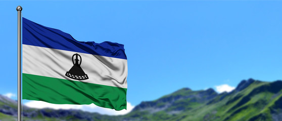 Lesotho flag waving in the blue sky with green fields at mountain peak background. Nature theme.