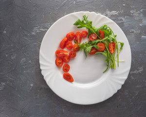 Sliced cherry tomatoes and fresh arugula leaves on a white plate.