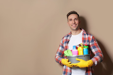 Man with basin of detergents on color background. Space for text