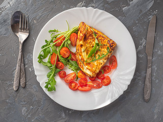 Light omelet breakfast with greens, cherry tomatoes on a large white plate on a gray background, shot from close range, top view. Leaves of fresh arugula.