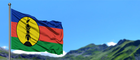 New Caledonia flag waving in the blue sky with green fields at mountain peak background. Nature theme.