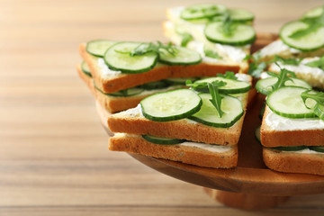 Wooden stand with traditional English cucumber sandwiches on table, closeup