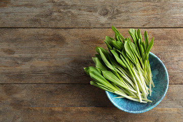 Bowl with wild garlic or ramson on wooden table, top view. Space for text