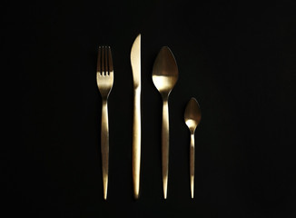 Set of gold cutlery on black background, flat lay