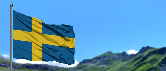 Sweden flag waving in the blue sky with green fields at mountain peak background. Nature theme.