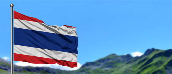 Obraz premium Thailand flag waving in the blue sky with green fields at mountain peak background. Nature theme.