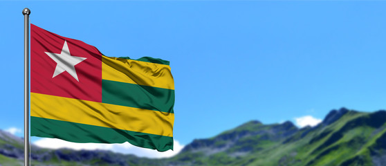 Togo flag waving in the blue sky with green fields at mountain peak background. Nature theme.