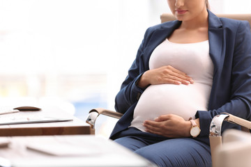 Young pregnant woman in suit at workplace, closeup. Space for text