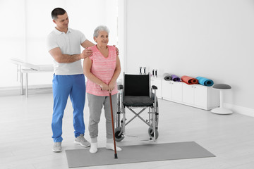 Fototapeta na wymiar Professional physiotherapist working with elderly patient in rehabilitation center. Space for text