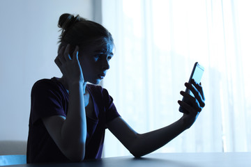 Shocked teenage girl with smartphone at table indoors. Danger of internet