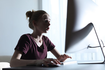 Shocked teenage girl using computer at table indoors. Danger of internet