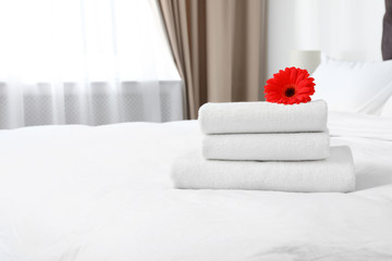 Stack of fresh towels with flower on bed indoors. Space for text