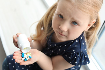 Little child with pills indoors, above view. Danger of medicament intoxication