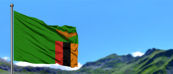 Zambia flag waving in the blue sky with green fields at mountain peak background. Nature theme. © sezerozger
