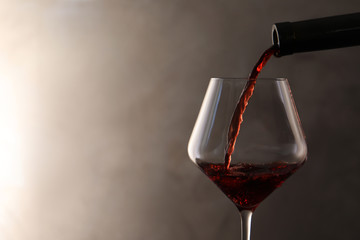 Pouring red wine from bottle into glass on color background. Space for text