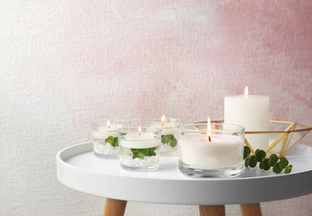 Composition with burning aromatic candles and eucalyptus on table near color wall. Space for text