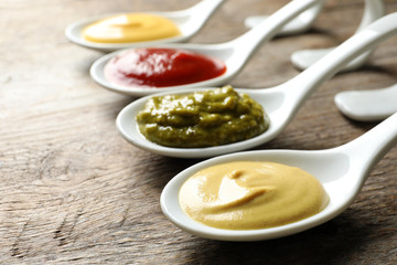 Spoons with different sauces on wooden background