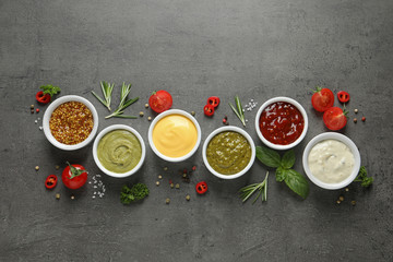 Bowls with different sauces and ingredients on gray background, flat lay