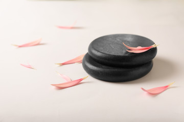 Stacked spa stones with flower petals on light background. Space for text
