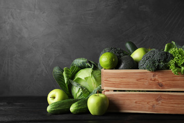 Wooden crate, fresh green fruits and vegetables on dark background. Space for text