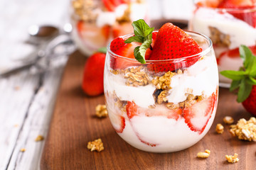 Healthy breakfast of strawberry parfaits made with fresh fruit, yogurt and granola over a rustic white table. Shallow depth of field with selective focus on glass jar in front. Blurred background. - Powered by Adobe
