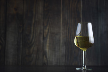 Transparent bottle of white dry wine on the table. White wine glass on a wooden background.