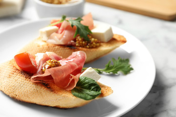Plate of tasty bruschettas with prosciutto on table, closeup
