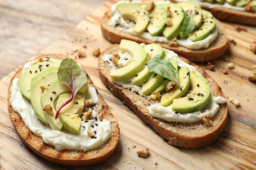 Delicious bruschettas with avocado served on wooden board, closeup