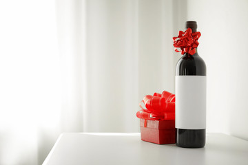Bottle of wine and gift box on table in light room. Space for text