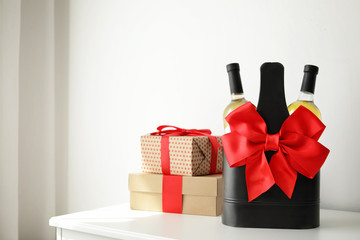 Bottles of wine in holder with bow and gift boxes on table in light room. Space for text