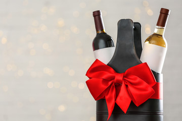 Bottles of wine in holder with bow against blurred lights. Space for text