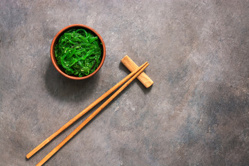 Wakame Chuka or seaweed salad with sesame seeds in bowl on dark brown rustic background. Traditional Japanese food. Top view, flat lay,copy space.