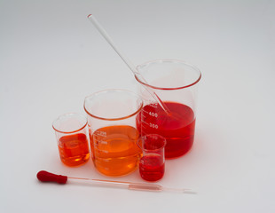 Four science beakers filled with orange and red liquid set to the left side of the screen on a white background with a dropper with a red bulb