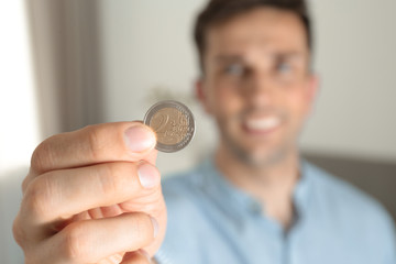 Young man holding coin at home, focus on hand