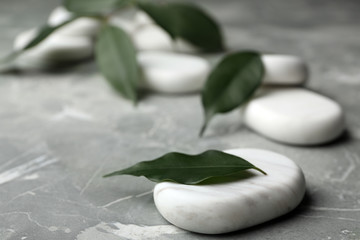 Fototapeta premium Spa stones and green leaves on grey background. Space for text