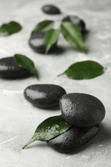 Wet spa stones and green leaves on grey background. Space for text