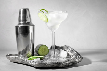 Composition with glass of cucumber martini on table against light background. Space for text