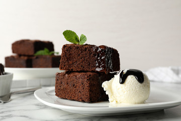 Plate with fresh brownies and ice-cream on table. Delicious chocolate pie