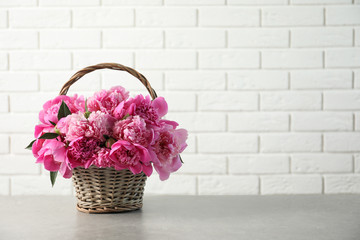 Wicker basket with fragrant peonies on table against brick wall, space for text. Beautiful spring...